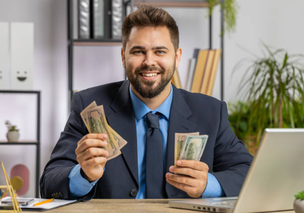 Rich young businessman working on laptop pc counting money cash, calculate earnings income profit at home office workplace. Professional manager freelancer man. Business people. Employment occupation