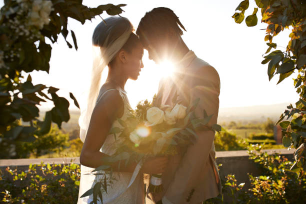Back lit young bride and groom touching foreheads standing at wedding altar during ceremony