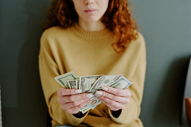 Person sitting down holding several dollar bills with both hands, intently focusing on counting cash, while wearing casual attire